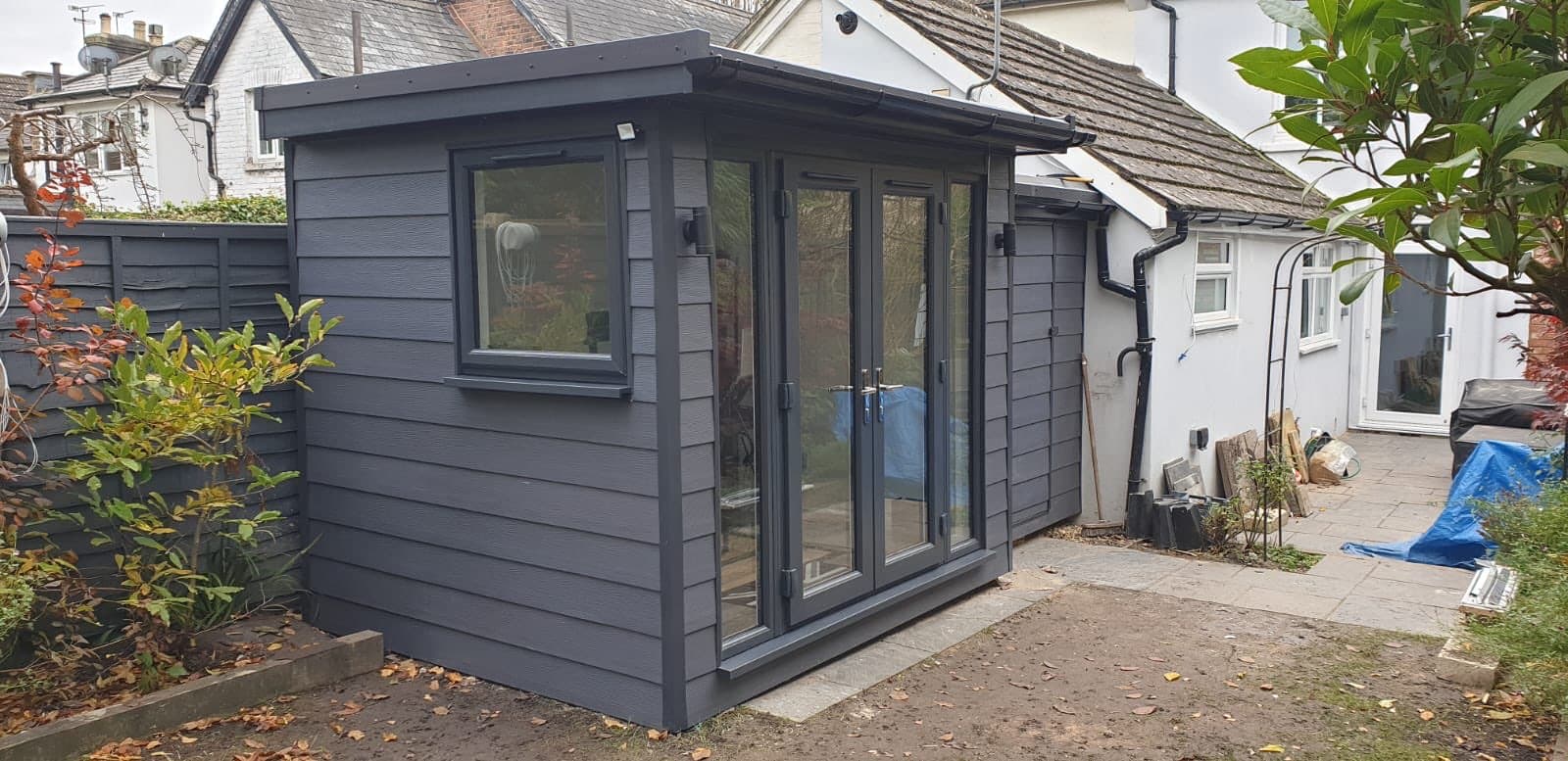 Anthracite composite garden office with a pent roof, French doors and a side window, built close to the house wall