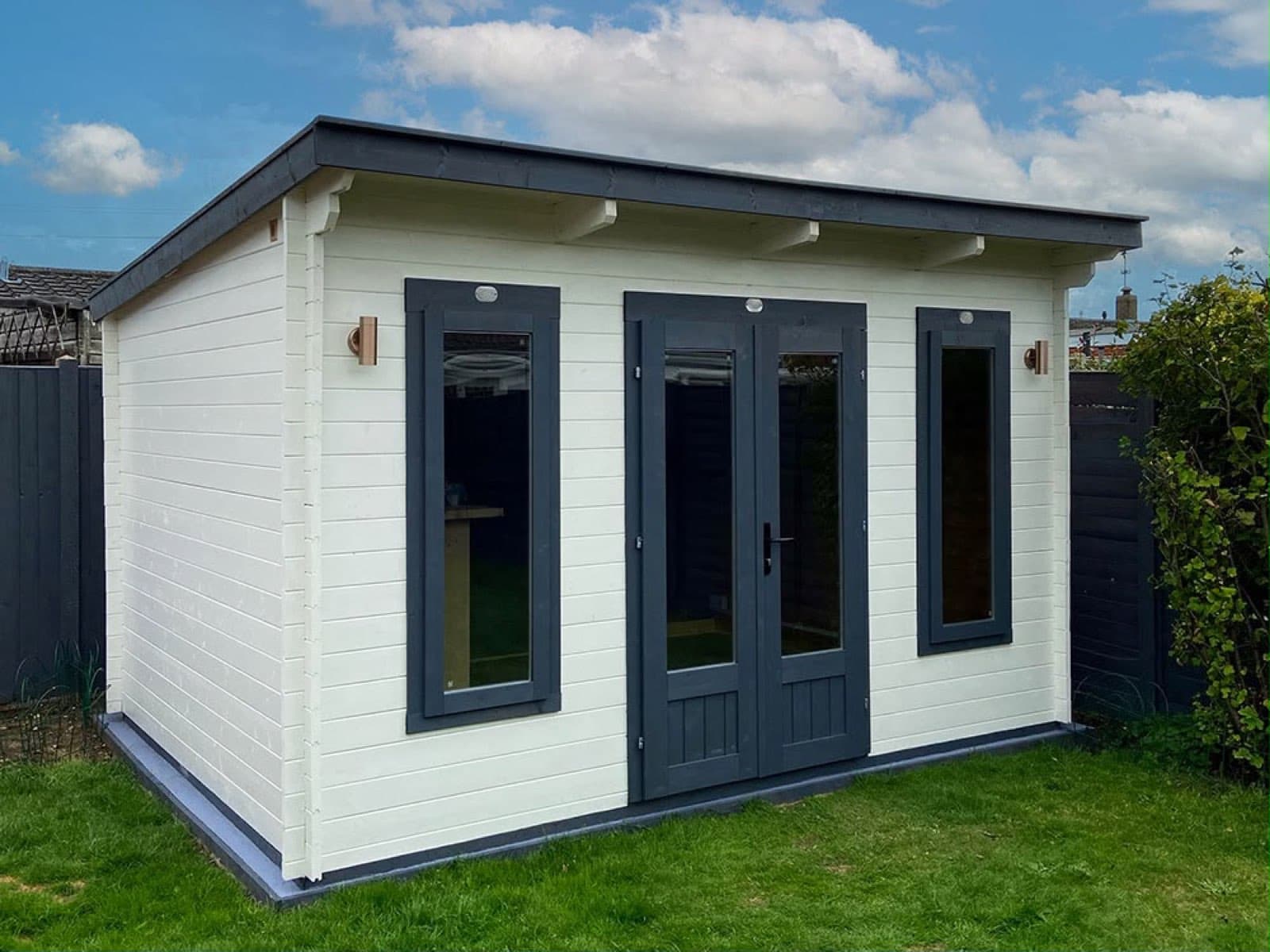 Cream painted pent log cabin with anthracite doors and window frames, on a lawn