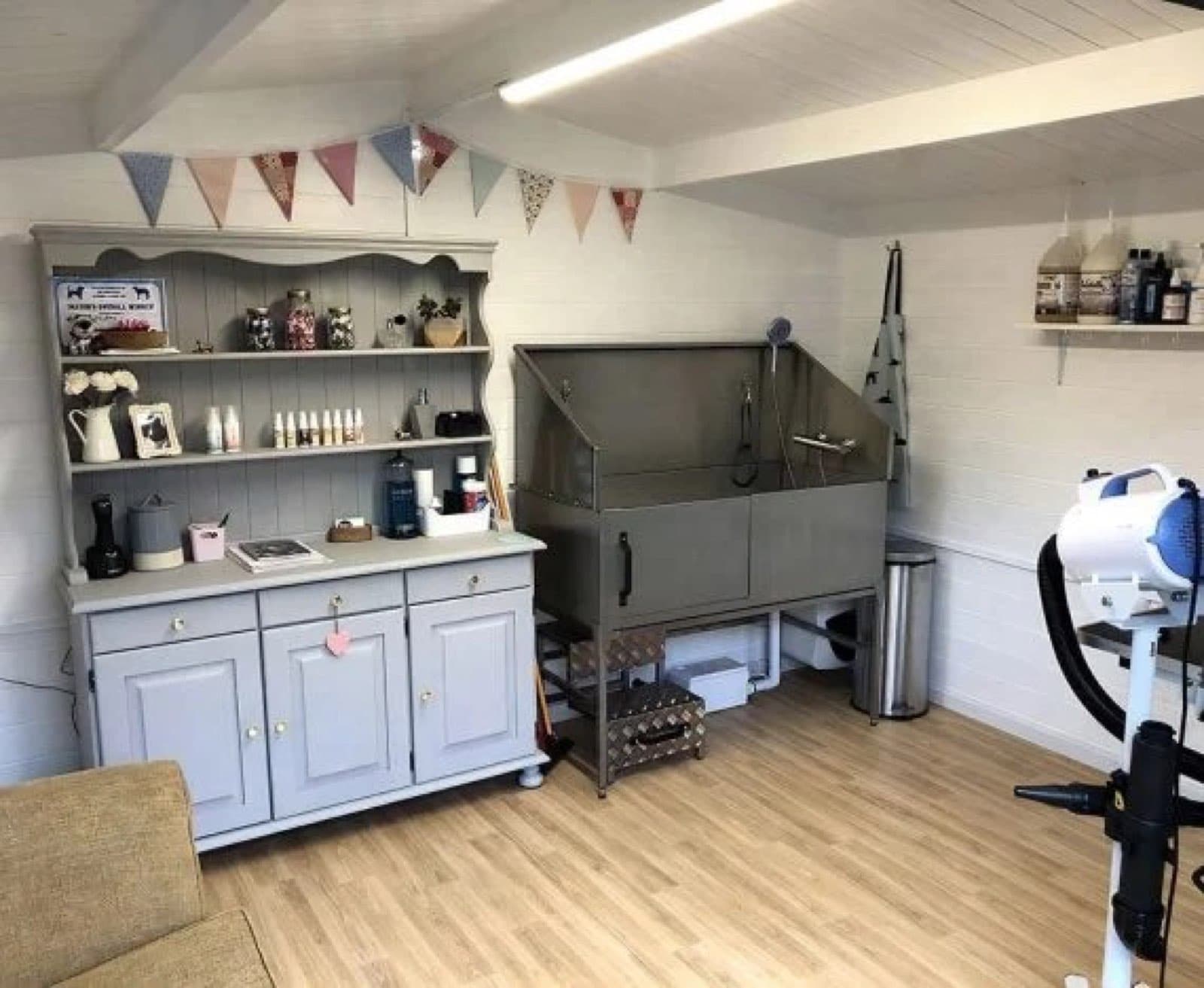 Inside a garden room fitted out as a dog grooming salon, with a stainless steel grooming bath, a painted dresser, bunting and a dryer