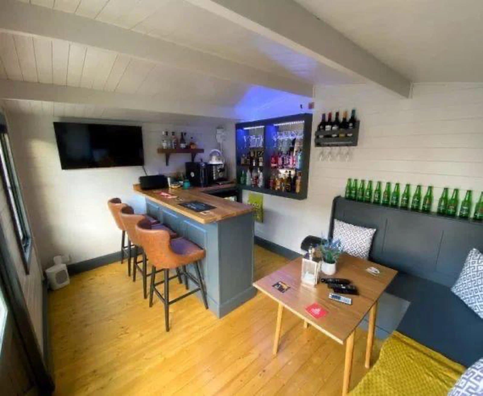 Inside a garden bar with a timber-topped counter, leather bar stools, a wall-mounted TV and bench seating