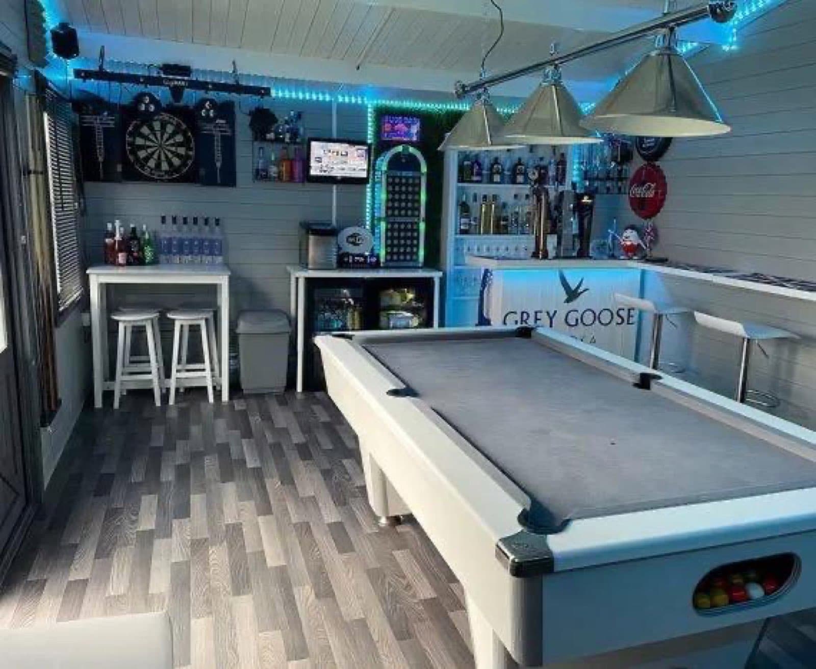 Inside a garden bar and games room with a pool table, dartboard, blue LED lighting and a bar with stools