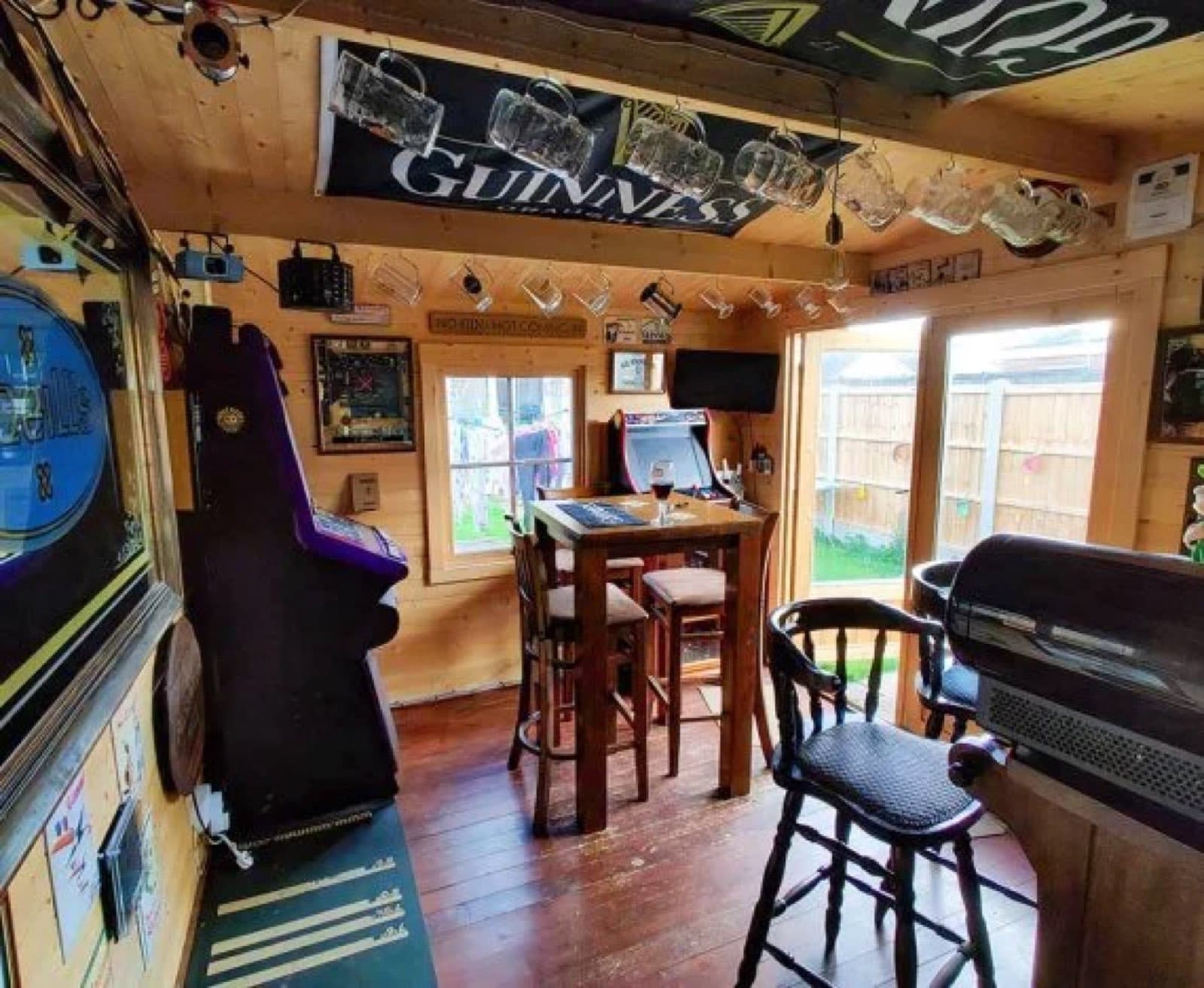 Inside a garden pub with a Guinness banner, an arcade machine, a dartboard and a high table with stools