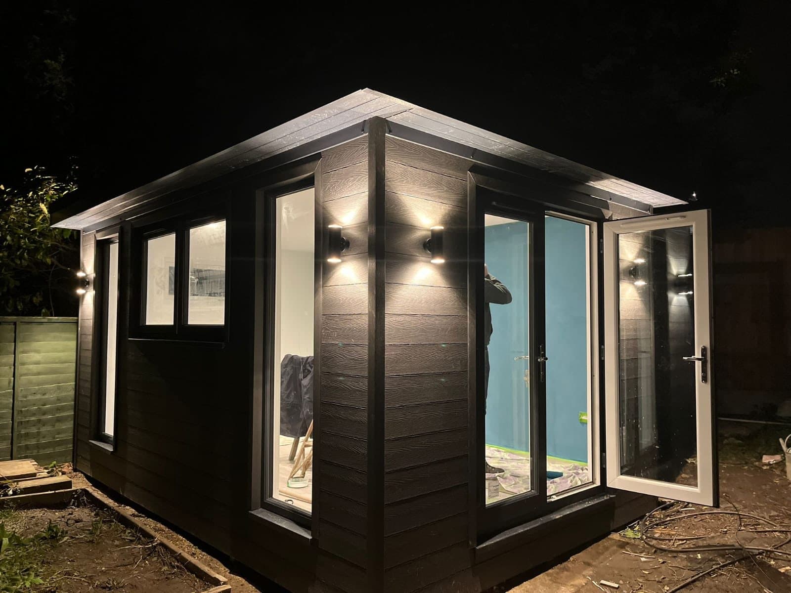 Dark garden room at night lit by wall downlights, with corner glazing and white uPVC doors, the interior mid-decoration