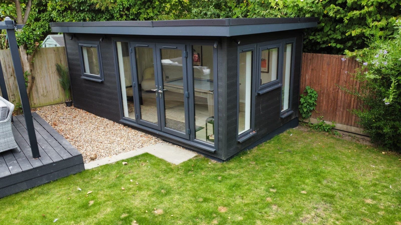 Graphite composite-clad garden room with white uPVC bifold doors and corner glazing, with a gravel border and decking alongside