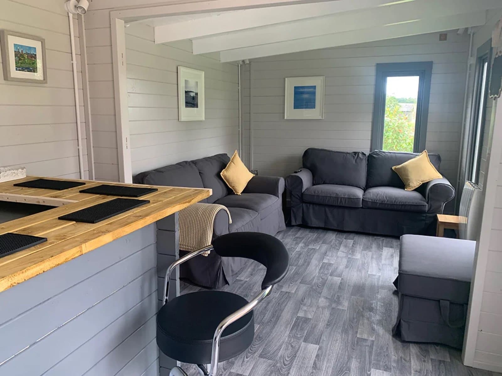 Inside a grey painted log cabin fitted out as a bar and lounge, with a timber bar counter, two grey sofas and gold cushions