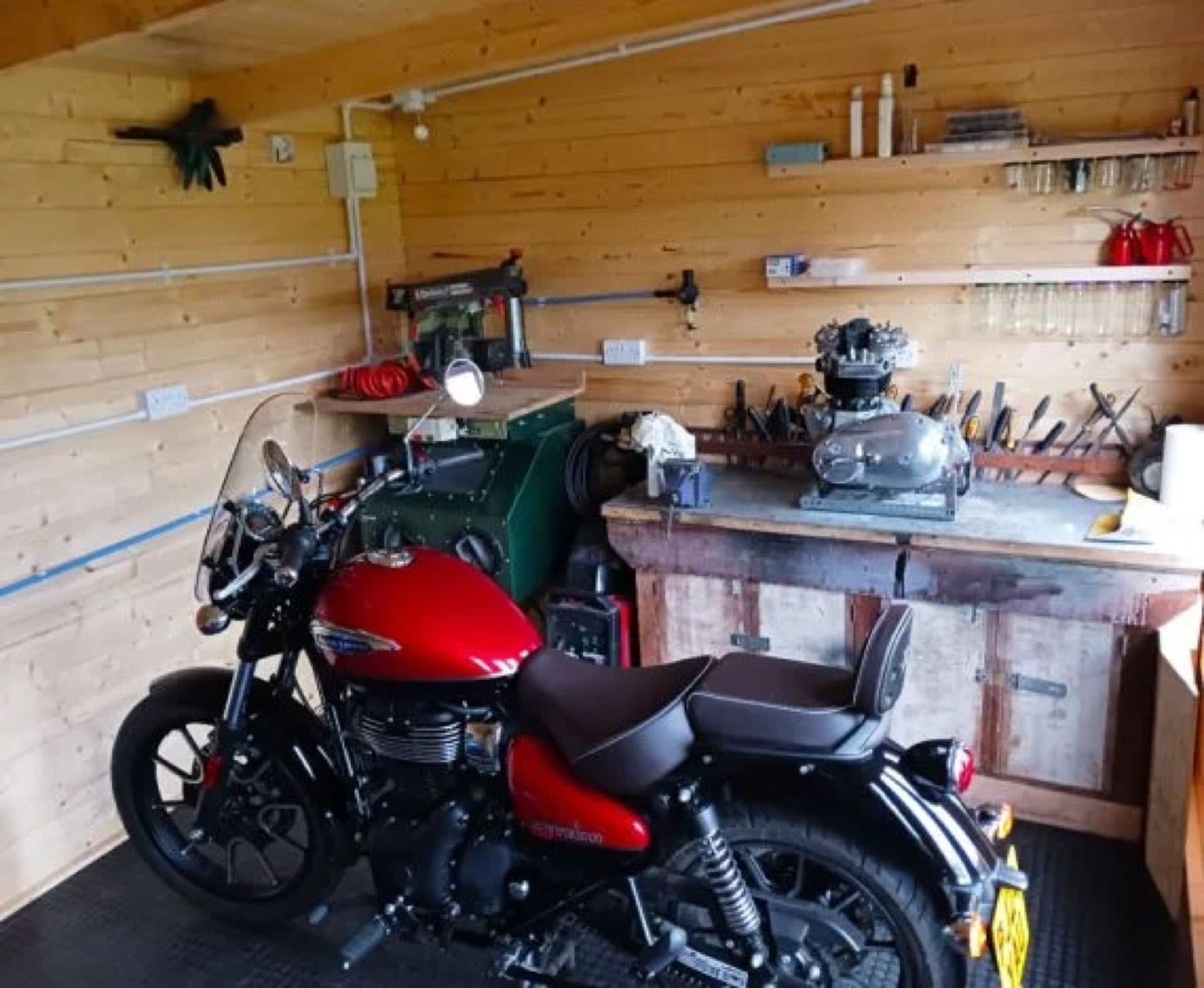 Inside a log cabin motorcycle workshop with a red motorbike, a workbench, hand tools and shelving