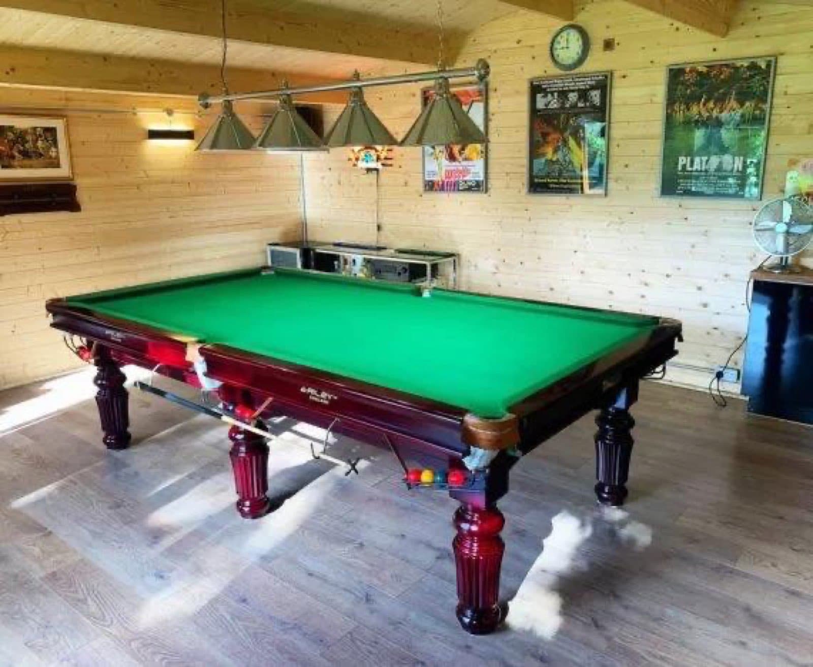 Inside a log cabin games room with a full-size snooker table, a run of pendant lights above it and framed film posters on the walls
