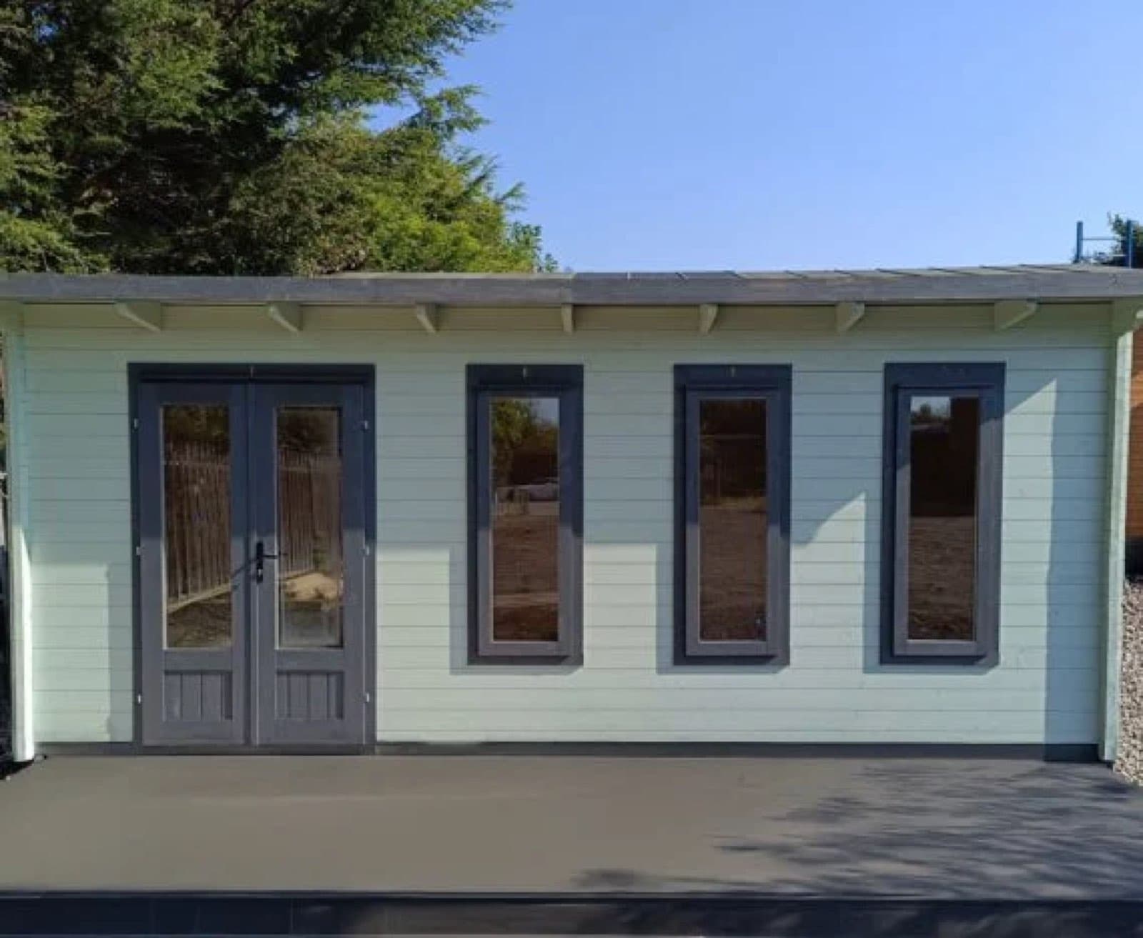 Pale green and white painted pent cabin with glazed double doors and three windows, on a concrete base