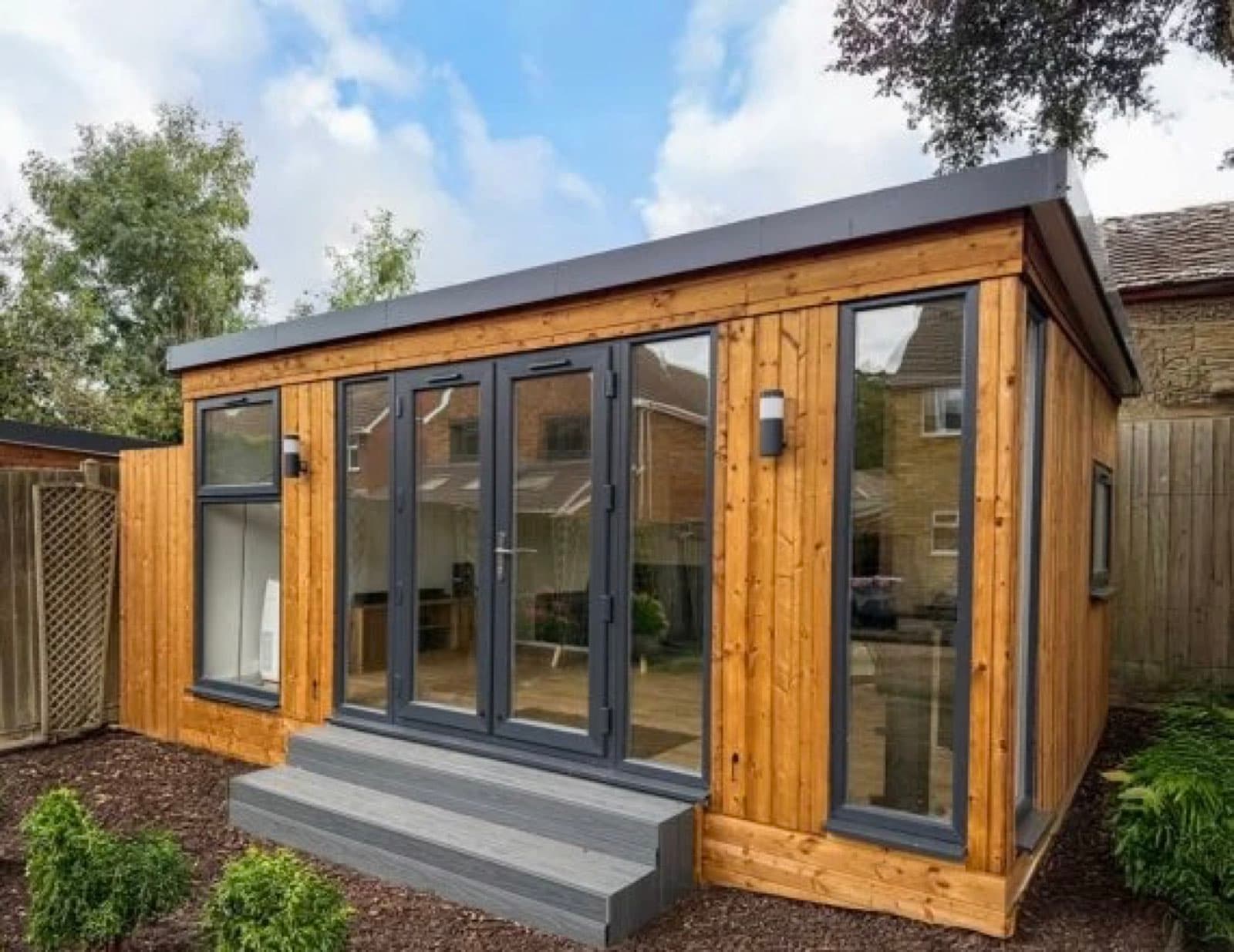 Timber-clad garden room with anthracite bifold doors and windows, composite steps up to the doors and a bark border