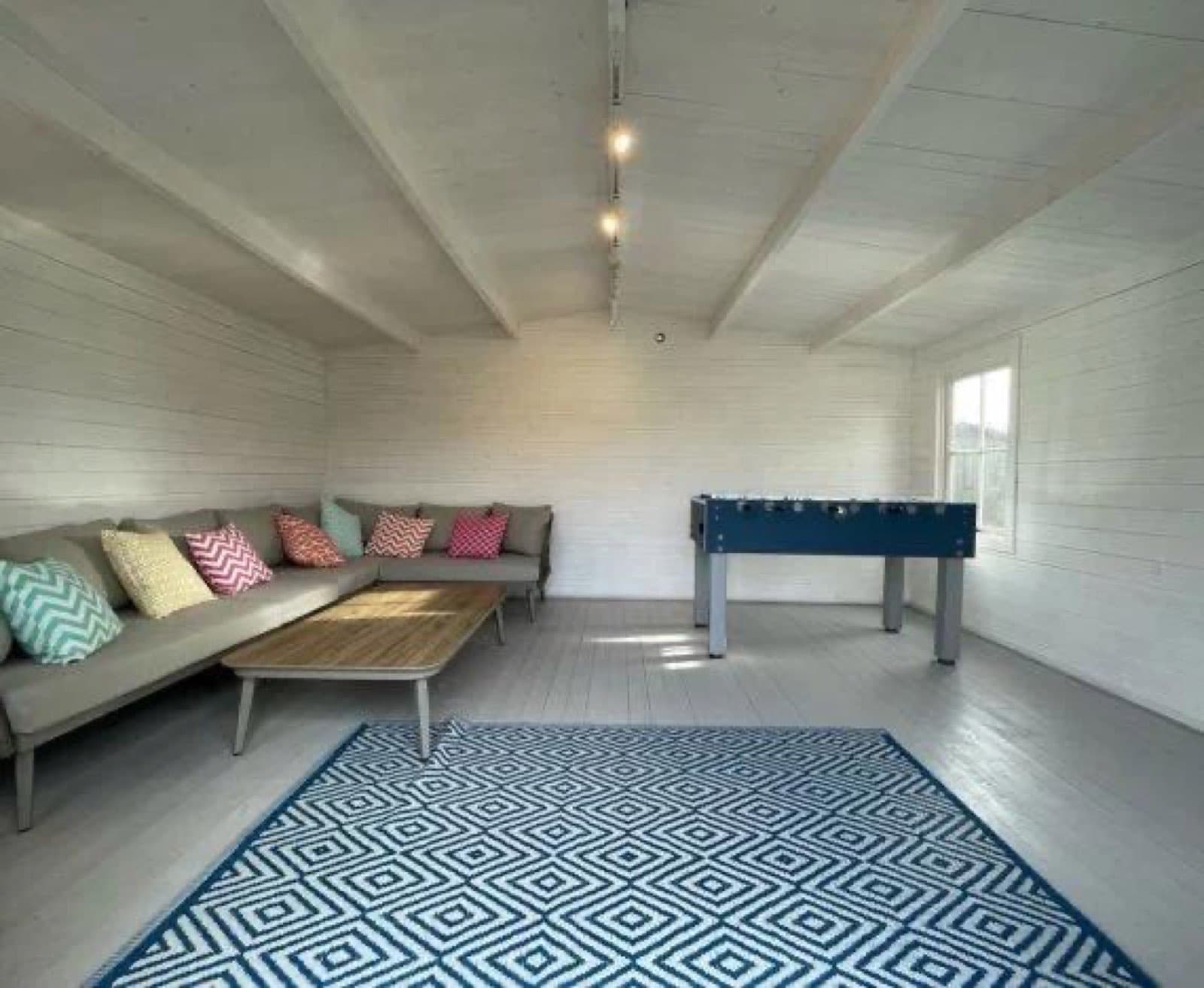 Inside a white painted garden room with a corner sofa, table football and a patterned rug