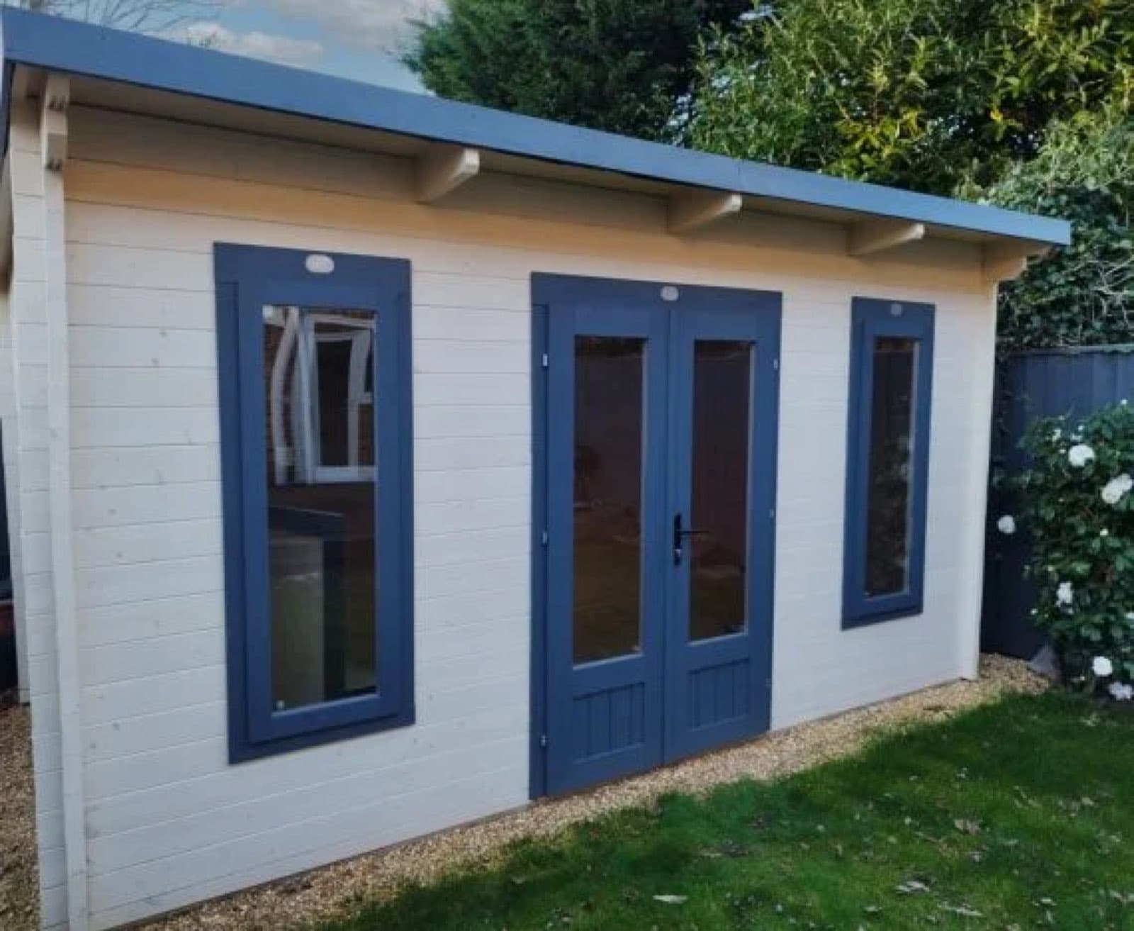 Cream cabin with blue painted doors and windows. Cream painted pent log cabin with blue doors and window surrounds, on a gravel border beside a lawn