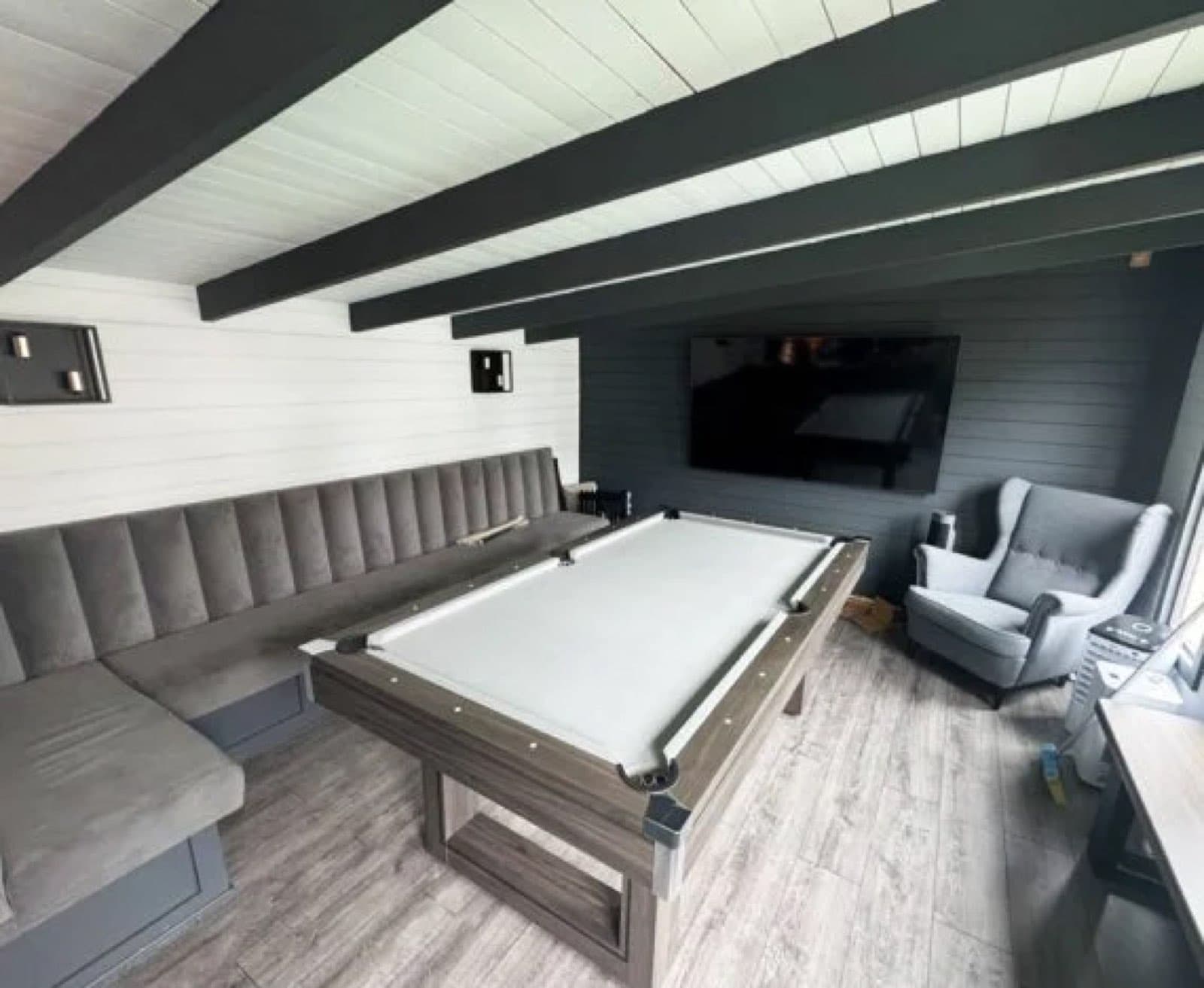 Games room with bench seating down one side. Inside a grey and white games room with a pool table, bench seating along one wall, a wall-mounted TV and an armchair