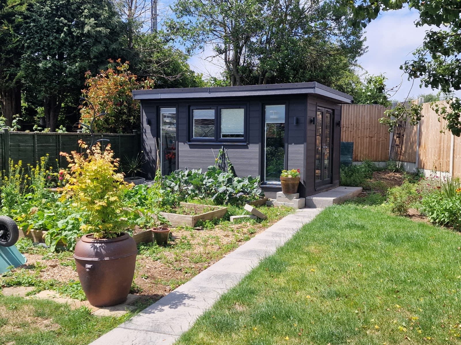 Grey garden room at the end of a working kitchen garden. Grey garden room at the end of a kitchen garden, with vegetable beds, a paved path and a lawn leading up to it