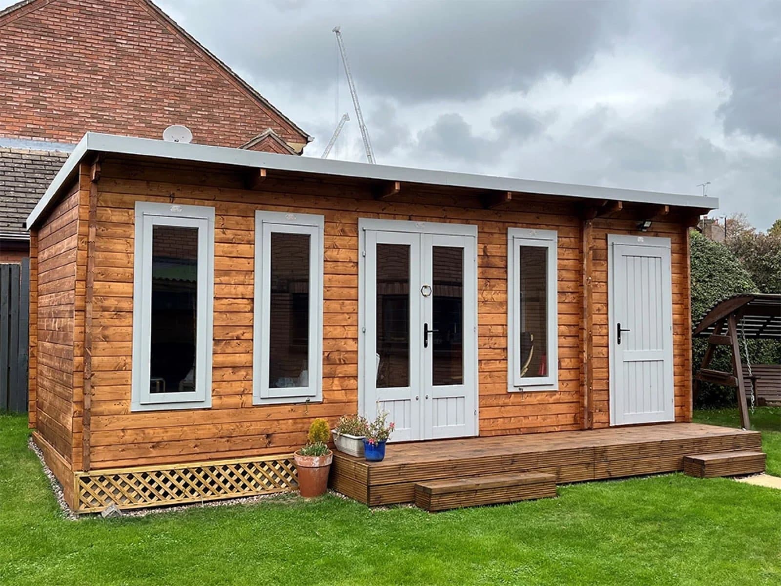 Honey cabin with a veranda across the front. Honey log cabin with white uPVC windows and doors and a timber veranda deck, on a lawn