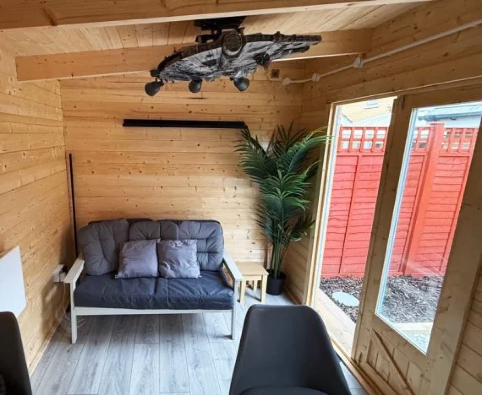 Log cabin lounge, finished and furnished. Inside a log cabin lounge with a sofa, a tall plant, a model aircraft hung from the ceiling and laminate flooring